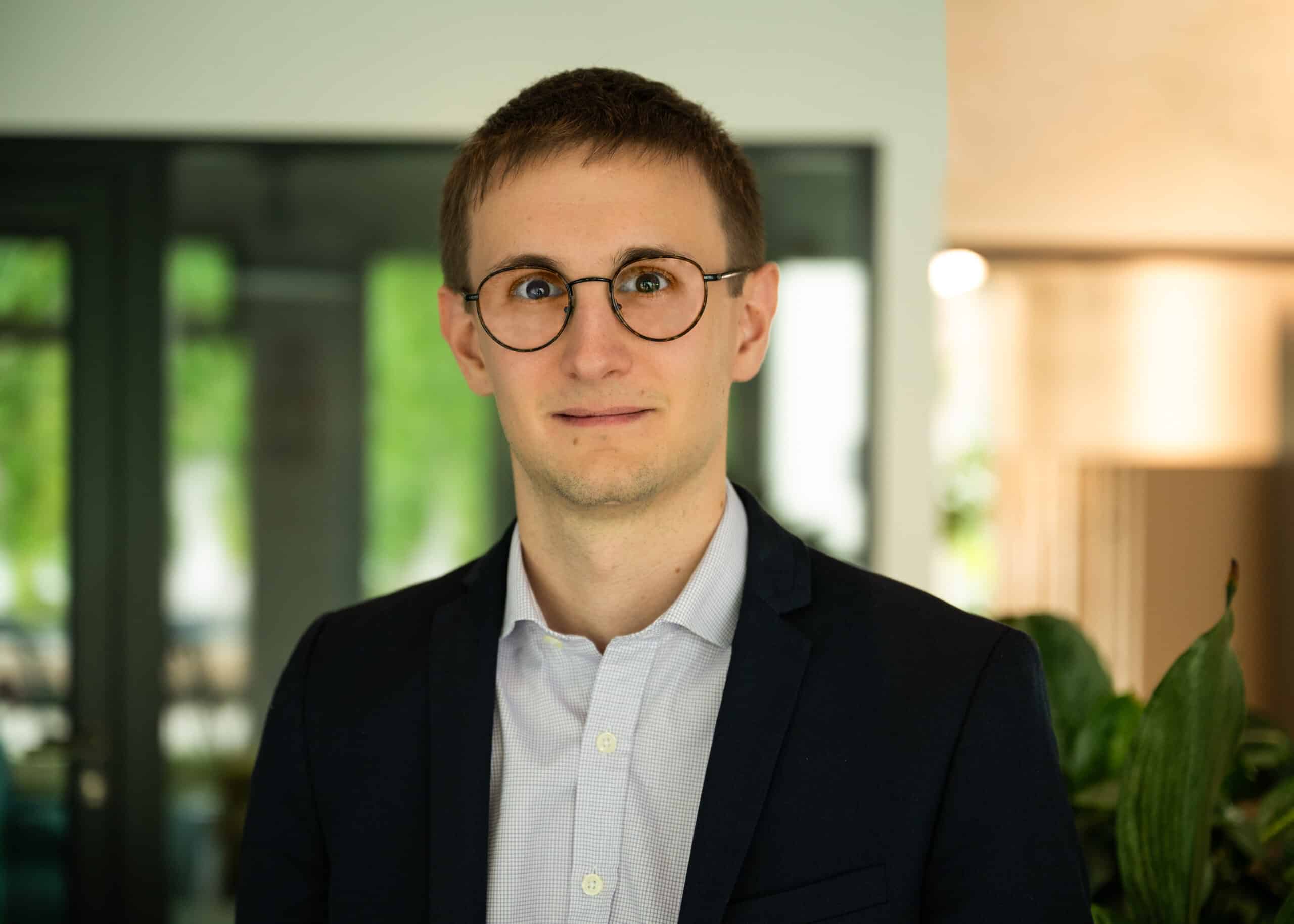 Lucas - Man in a suit with glasses in an office.